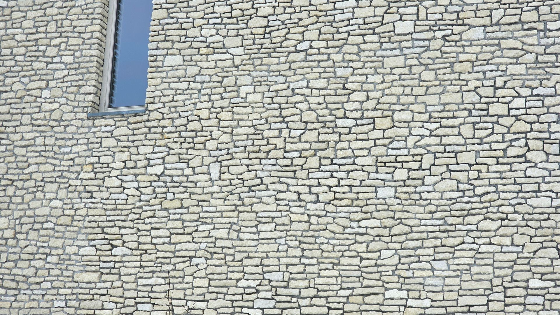 Stone wall with rectangular window revealing blue sky.
