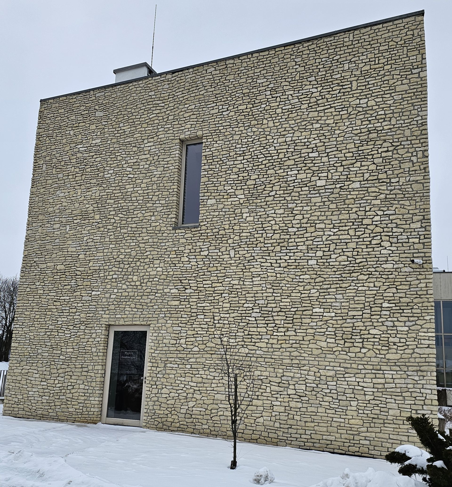 Stone building with a small door and window, set in snow. An antenna sits on the flat roof.