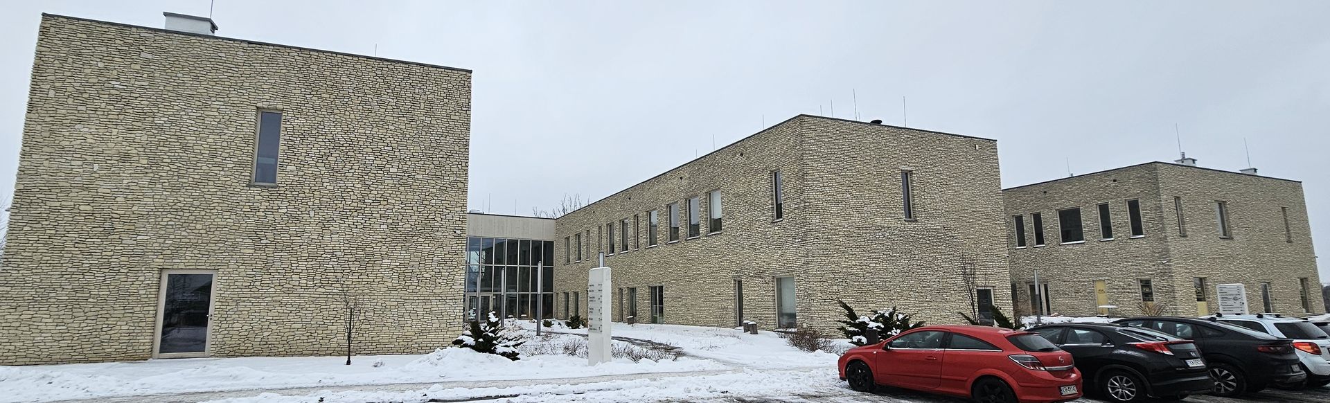 Stone-walled building on a snowy day. A red car is parked near the building.