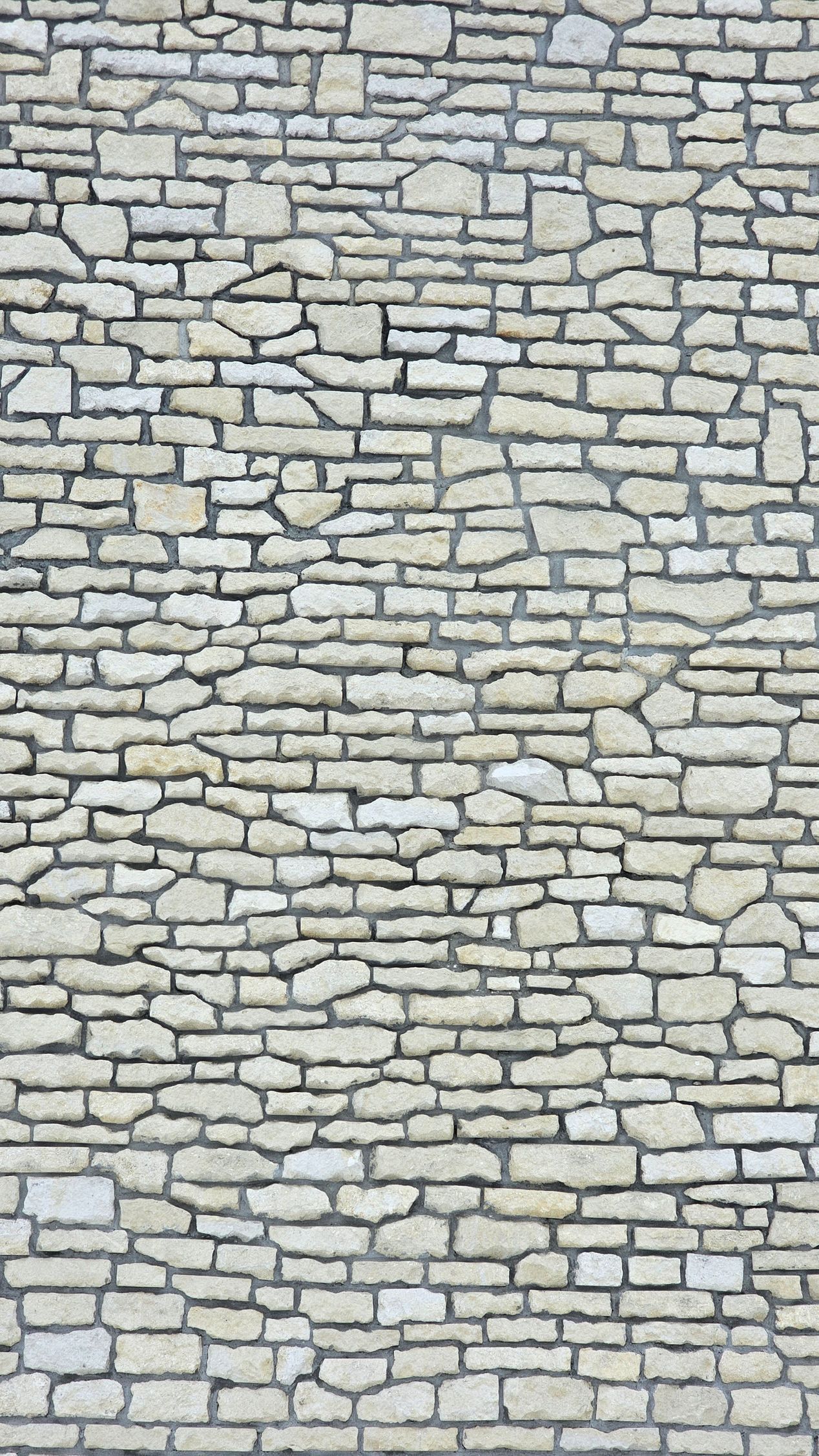Stone wall composed of various shapes and sizes of light-colored stones, mortared together.
