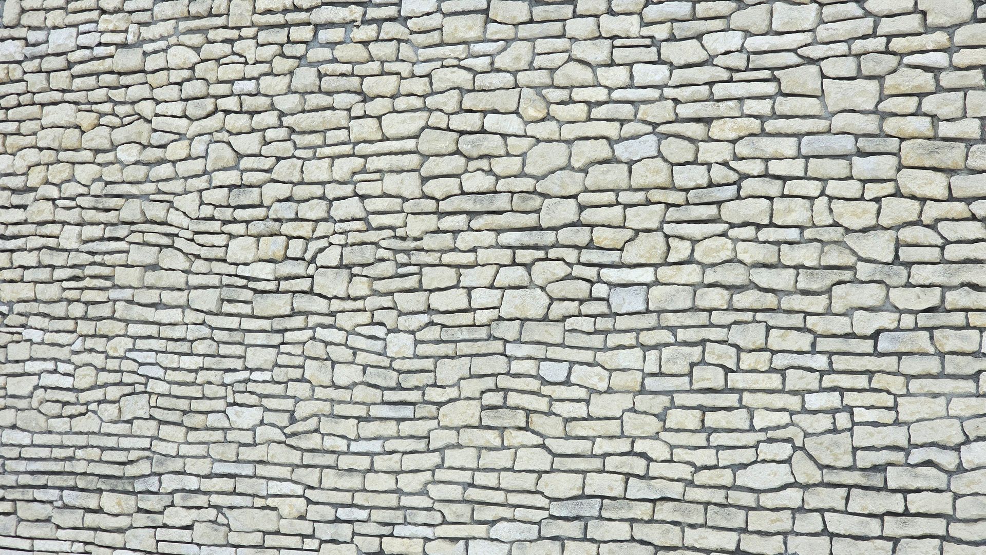 Stone wall with irregular, light-colored bricks and dark mortar.
