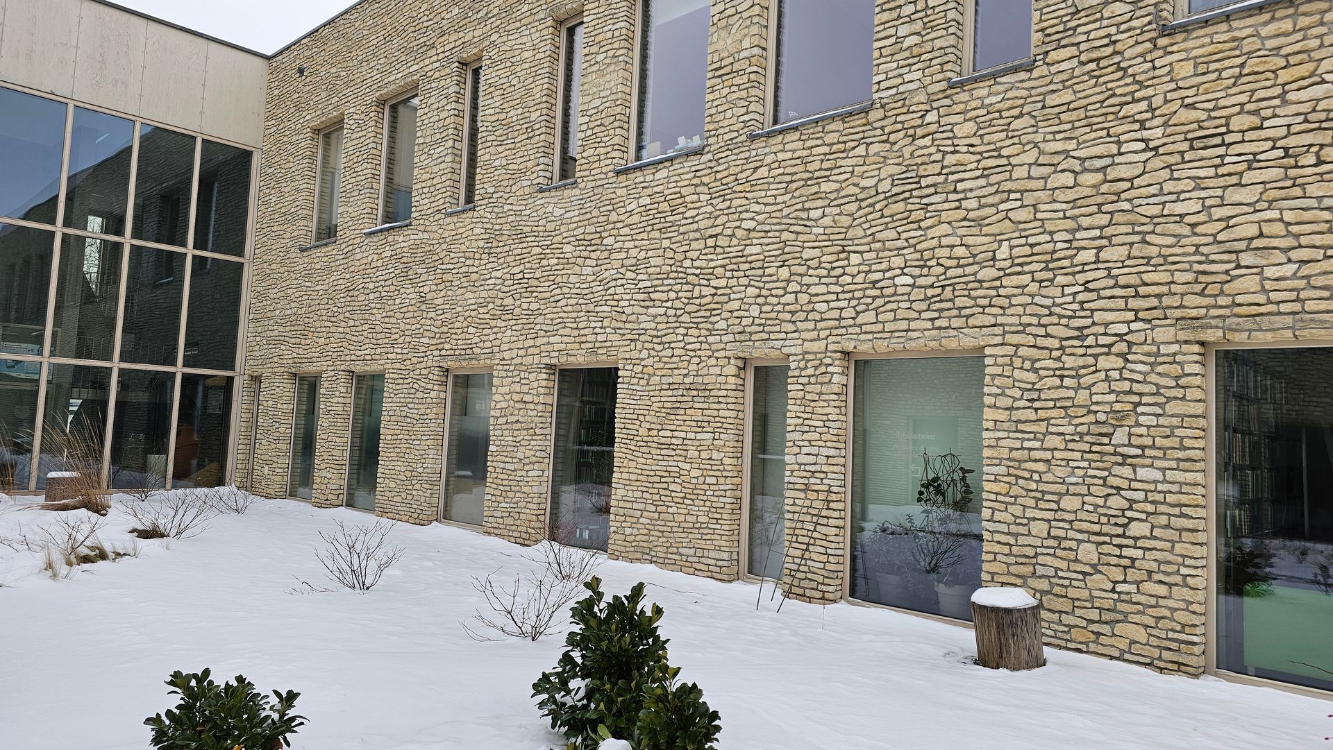Exterior of a building with stone facade, large windows, and snow on the ground.