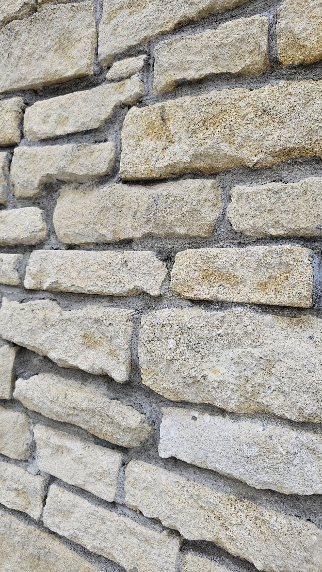 Stone wall with light-colored, rectangular blocks and gray mortar, viewed at an angle.
