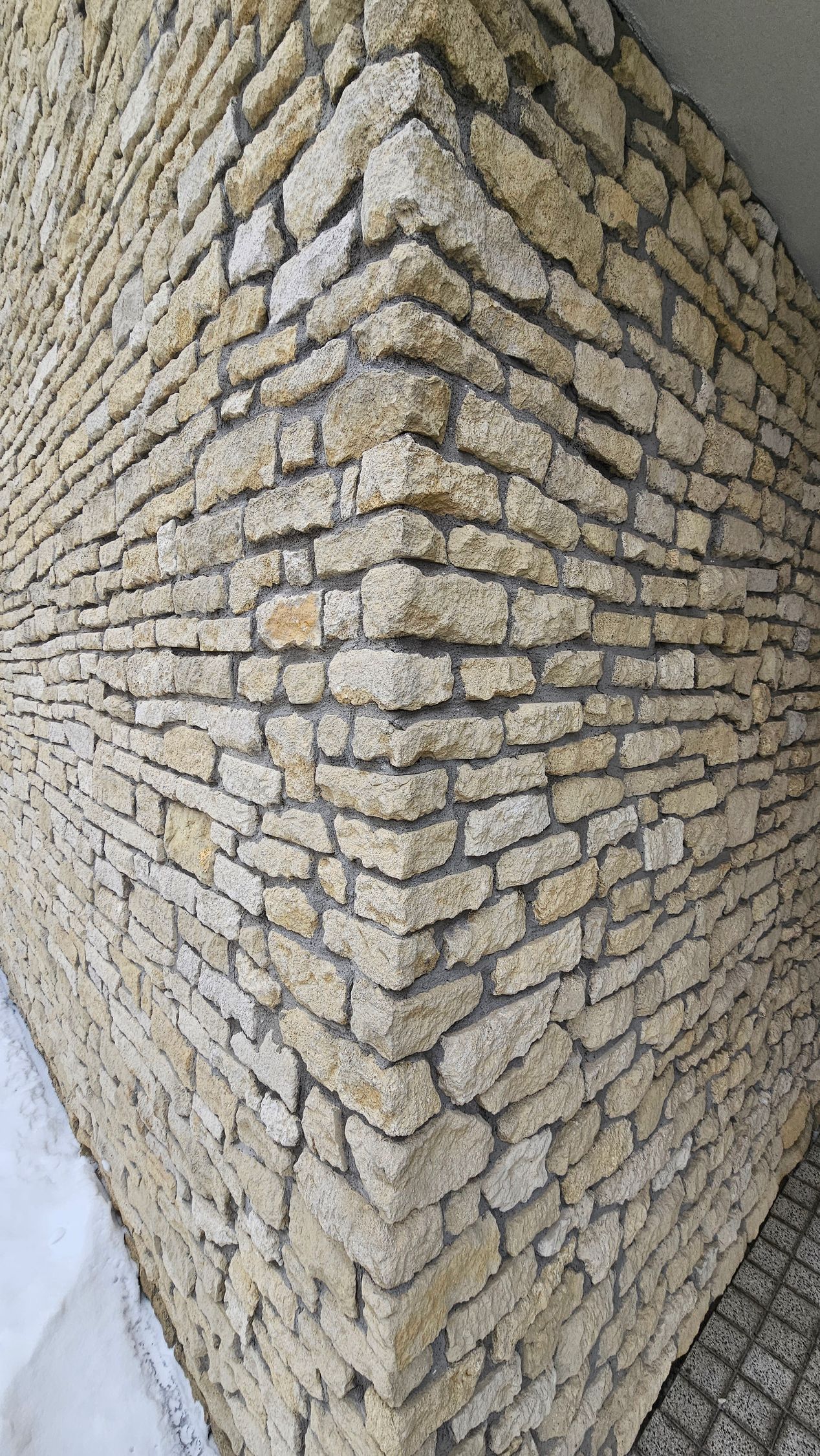 Corner of a stone wall, light brown, with horizontal rows of rectangular stones.