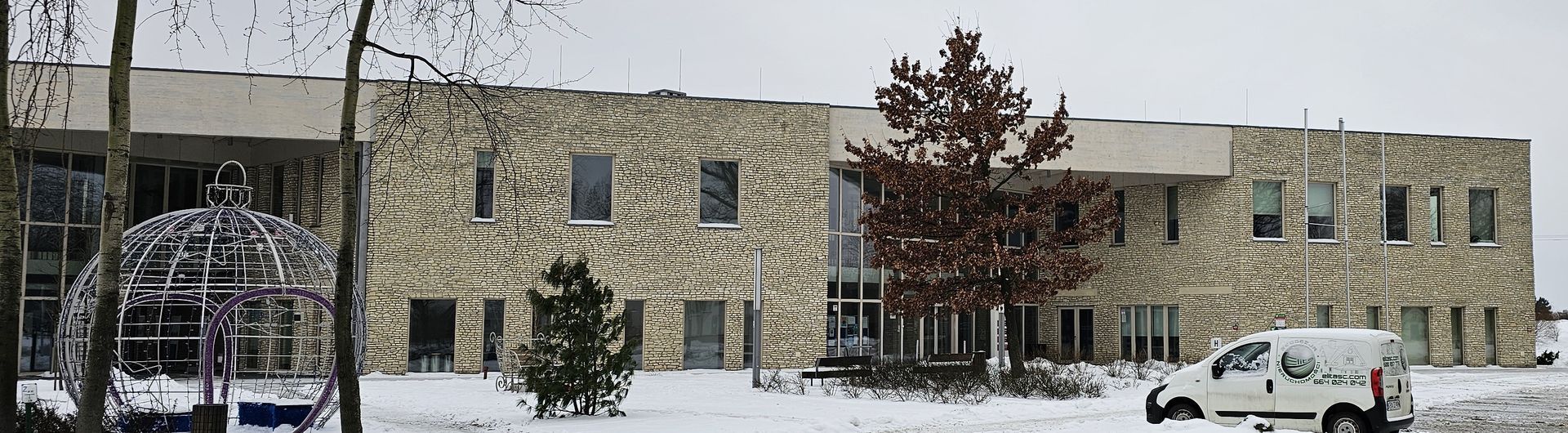 A two-story stone building covered in snow. A white van is parked in front of it.