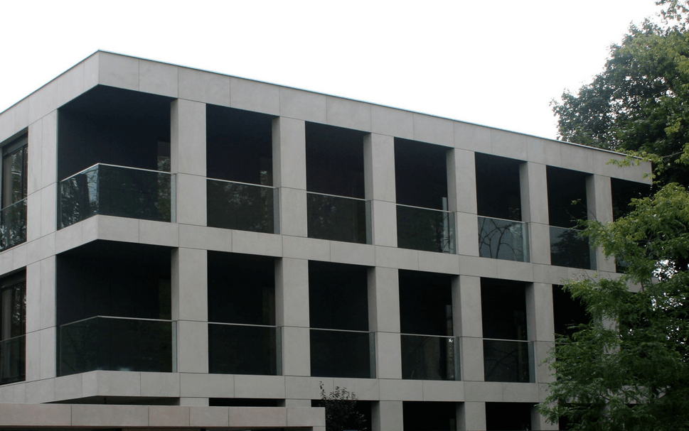 Modern three-story building with large square windows and glass balconies, beige exterior.
