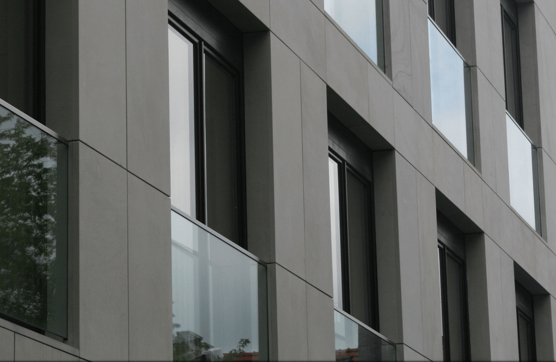 Gray building facade with rows of windows and glass balcony rails.