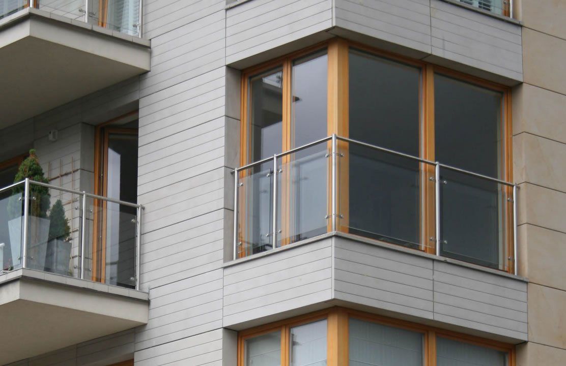 Modern apartment building with balconies, glass railings, and wood-framed windows.
