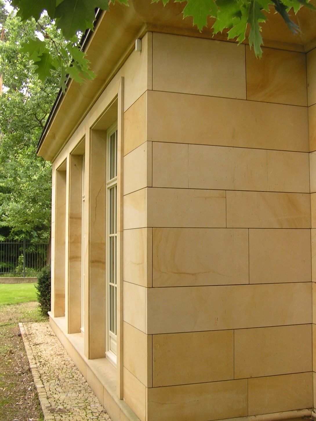 Tan stone building with rectangular blocks, windows, and a small roof.