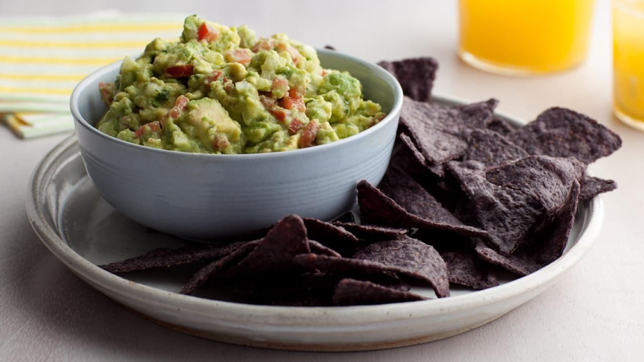 A bowl of guacamole is sitting on top of a plate of tortilla chips.