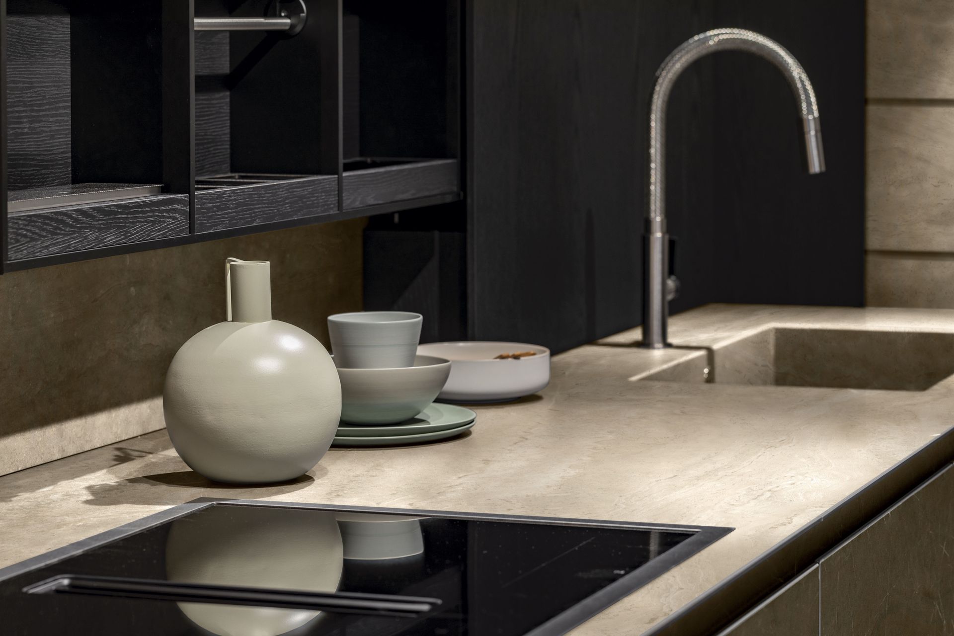 Piano di lavoro da cucina moderno con lavello, rubinetto, ciotola, tazza e vaso in tonalità neutre.