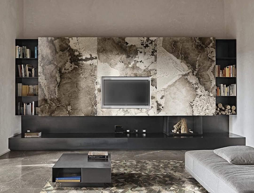 Soggiorno moderno con parete TV in marmo, mensole scure, consolle bassa e divano grigio.