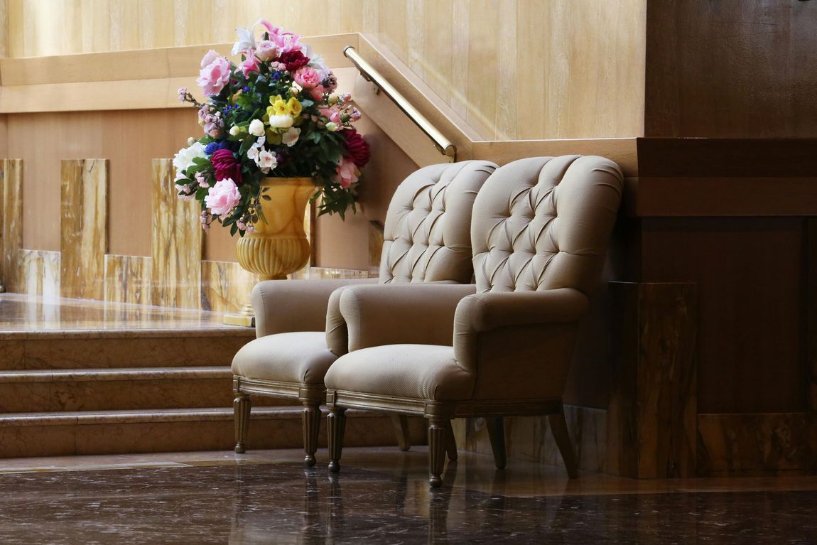 Due poltrone beige trapuntate accanto a una composizione floreale in una hall o in un atrio d'albergo elegante.