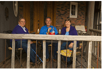 Three people are sitting at a table on a porch.