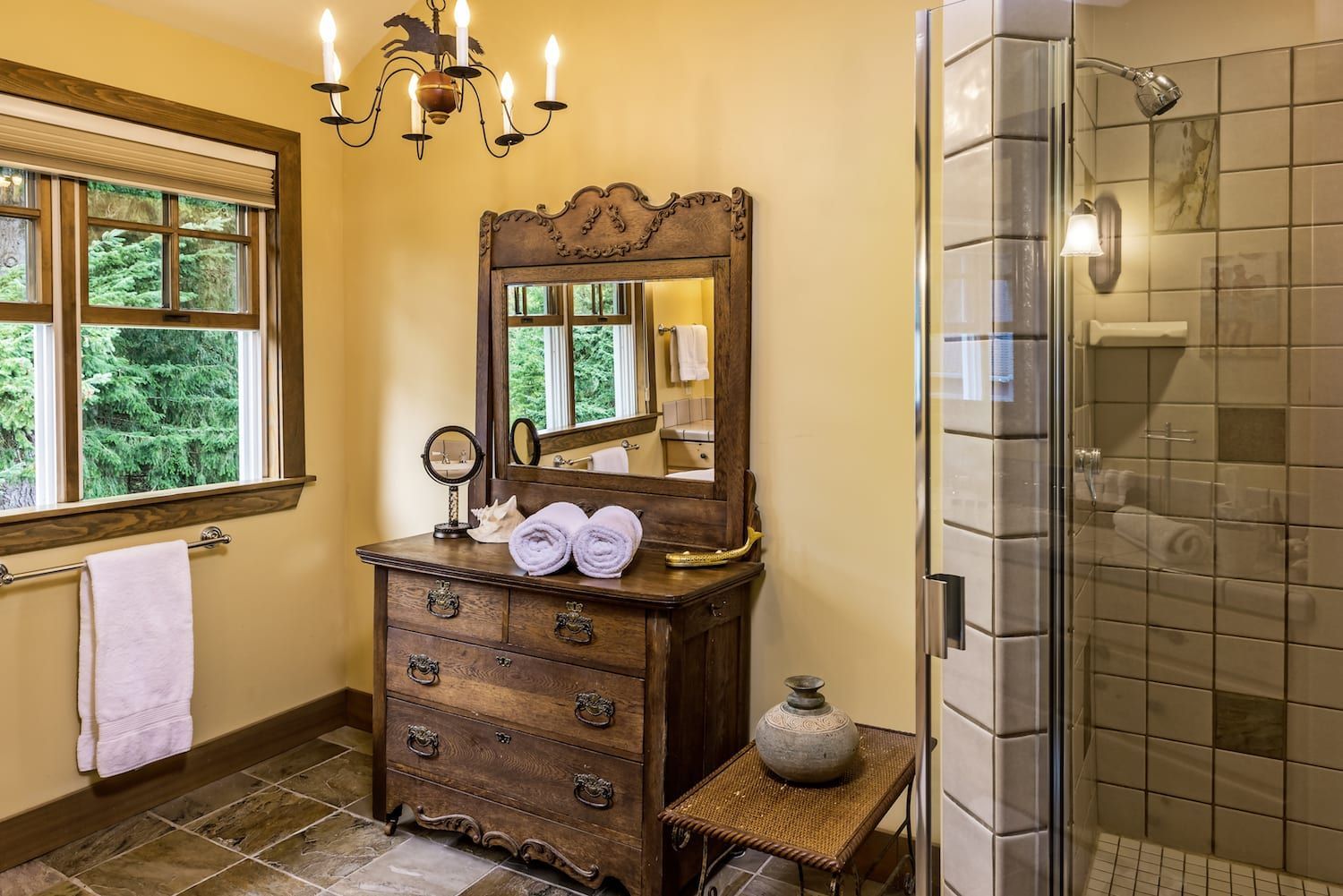 A bathroom with a dresser , mirror , and walk in shower.