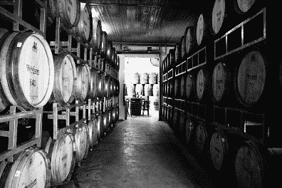 A black and white photo of a warehouse filled with lots of barrels.