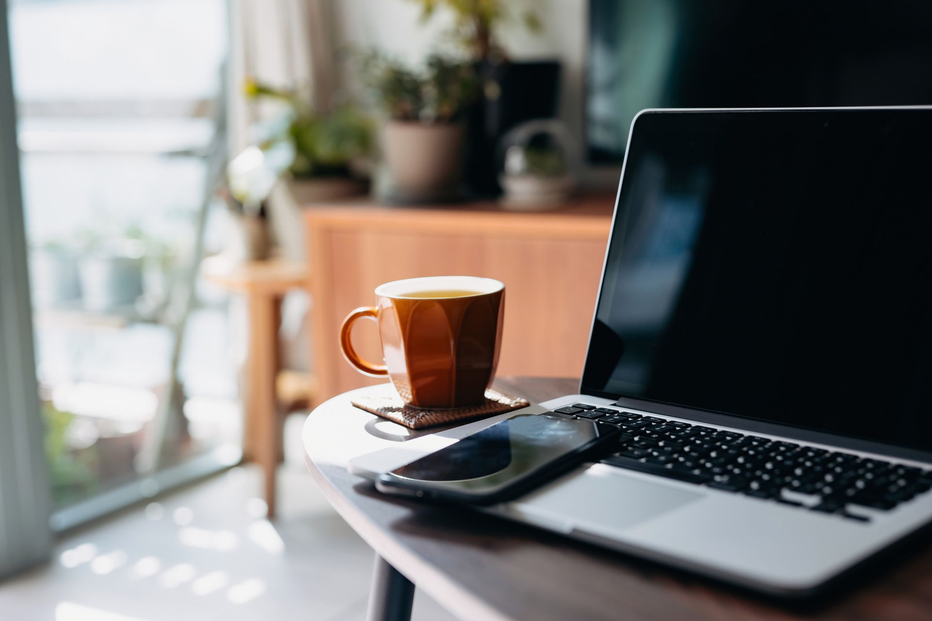 A cup of coffee is sitting on a table next to a laptop and a cell phone.