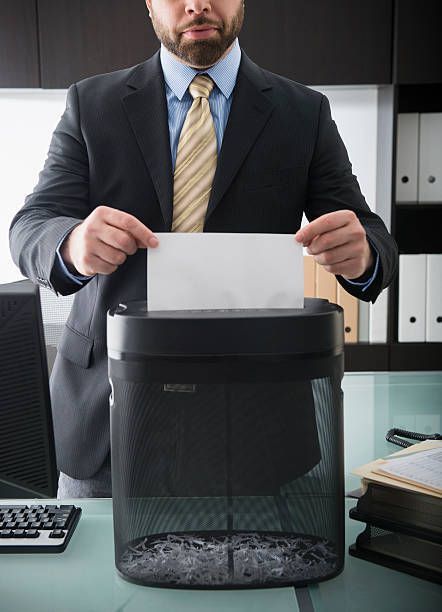 A man in a suit and tie is shredding paper in an office.