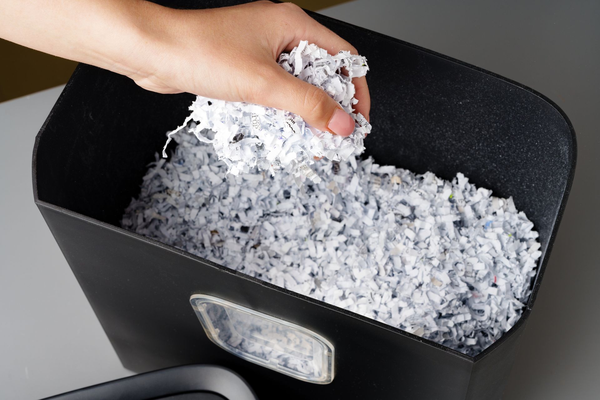A person is putting shredded paper into a trash can