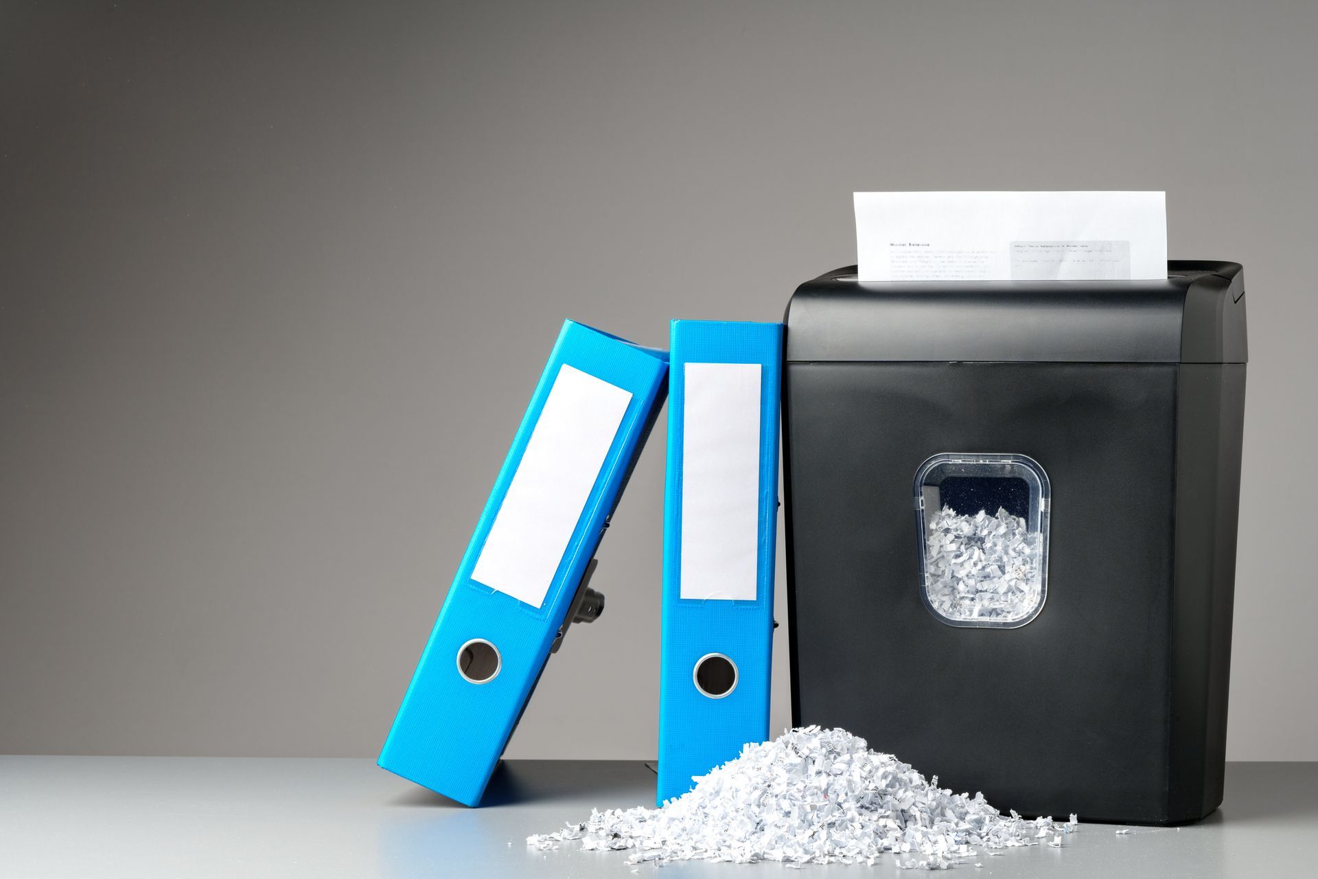 Two blue binders and a shredding machine on a table.
