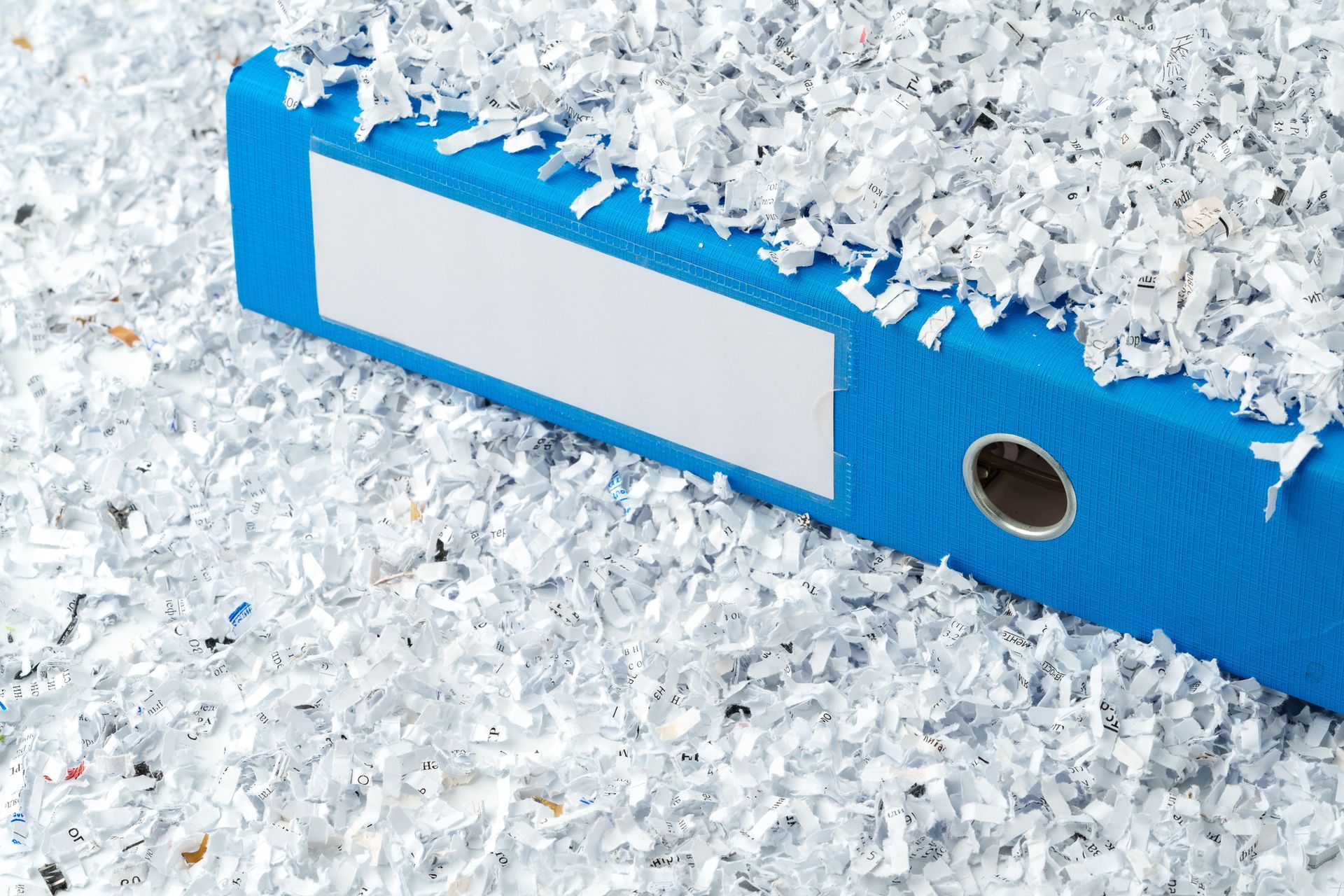 A blue binder is surrounded by shredded paper.