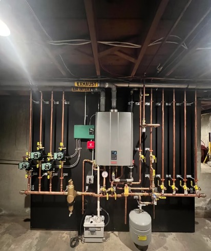 Mechanical room with copper piping, valves, a gray boiler, and a small tank against a dark wall.