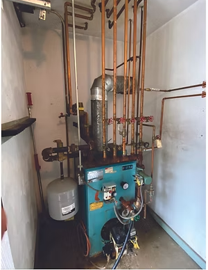 Boiler room with blue heating unit, copper pipes, and gray expansion tank in a narrow utility closet.