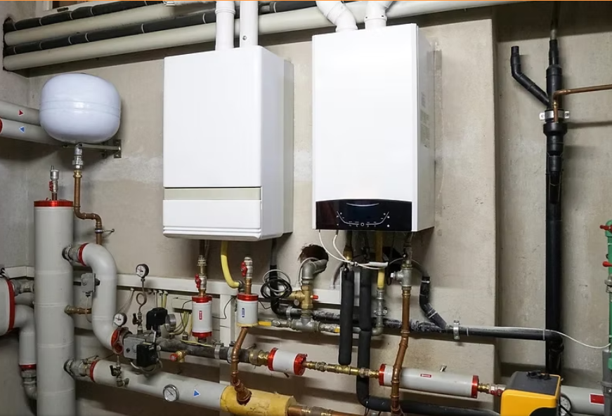 Boiler room with white wall-mounted units, pipes, valves, and a gray expansion tank against a basement wall