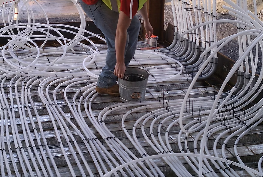 Construction worker pouring concrete over a dense network of white floor tubing