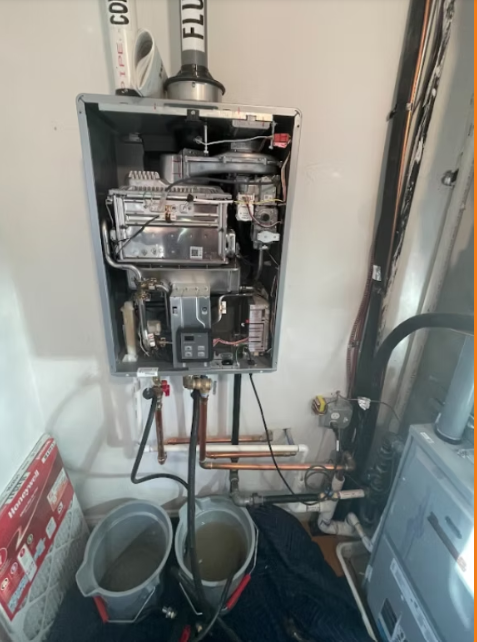 Open electrical breaker panel in utility closet with copper piping and buckets below
