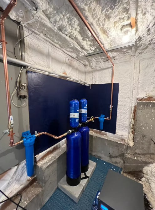 Industrial water treatment room with blue filter tanks and pipes under insulated ceiling utilities