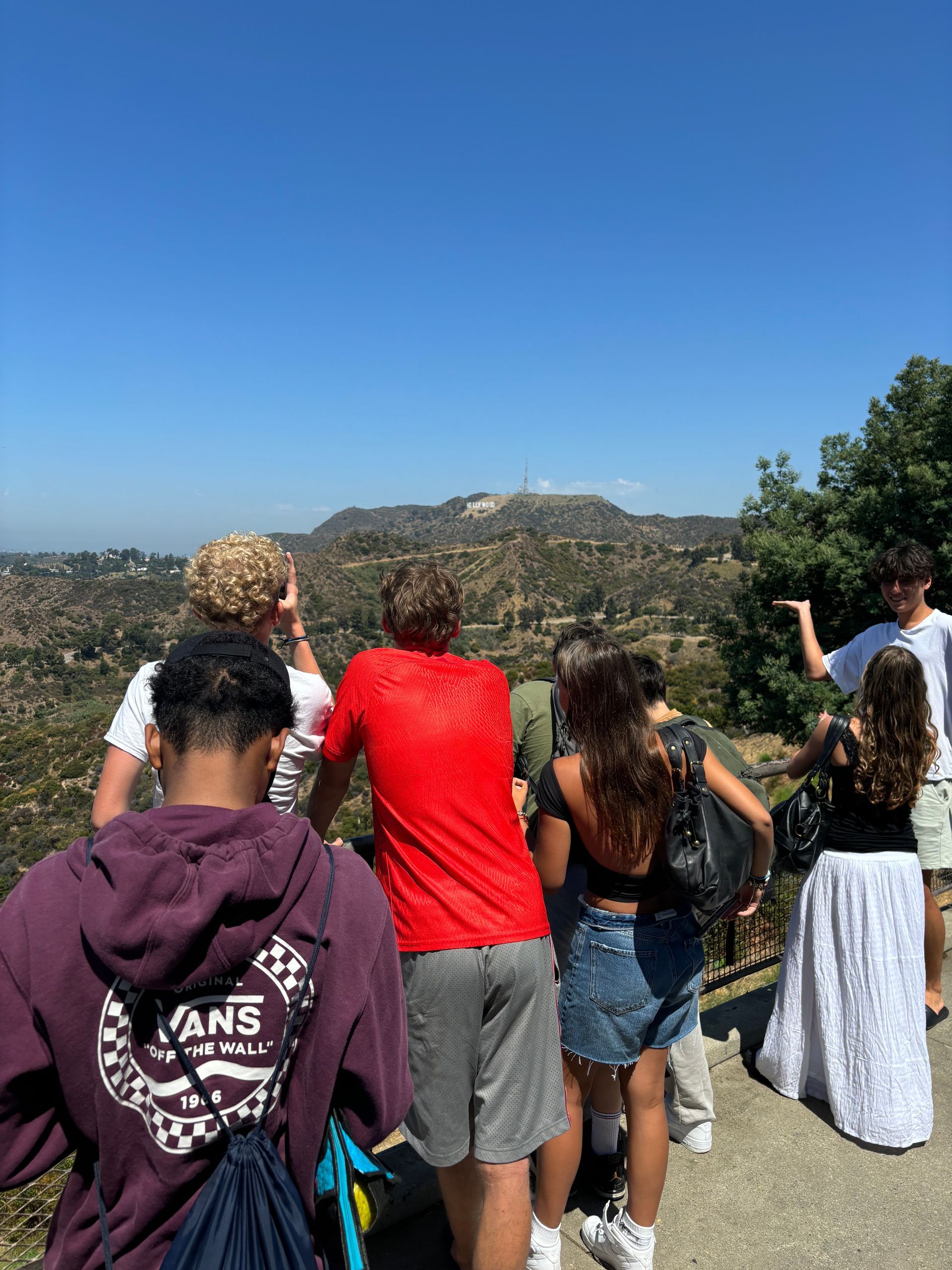 A group of people are standing on top of a hill looking at a mountain.