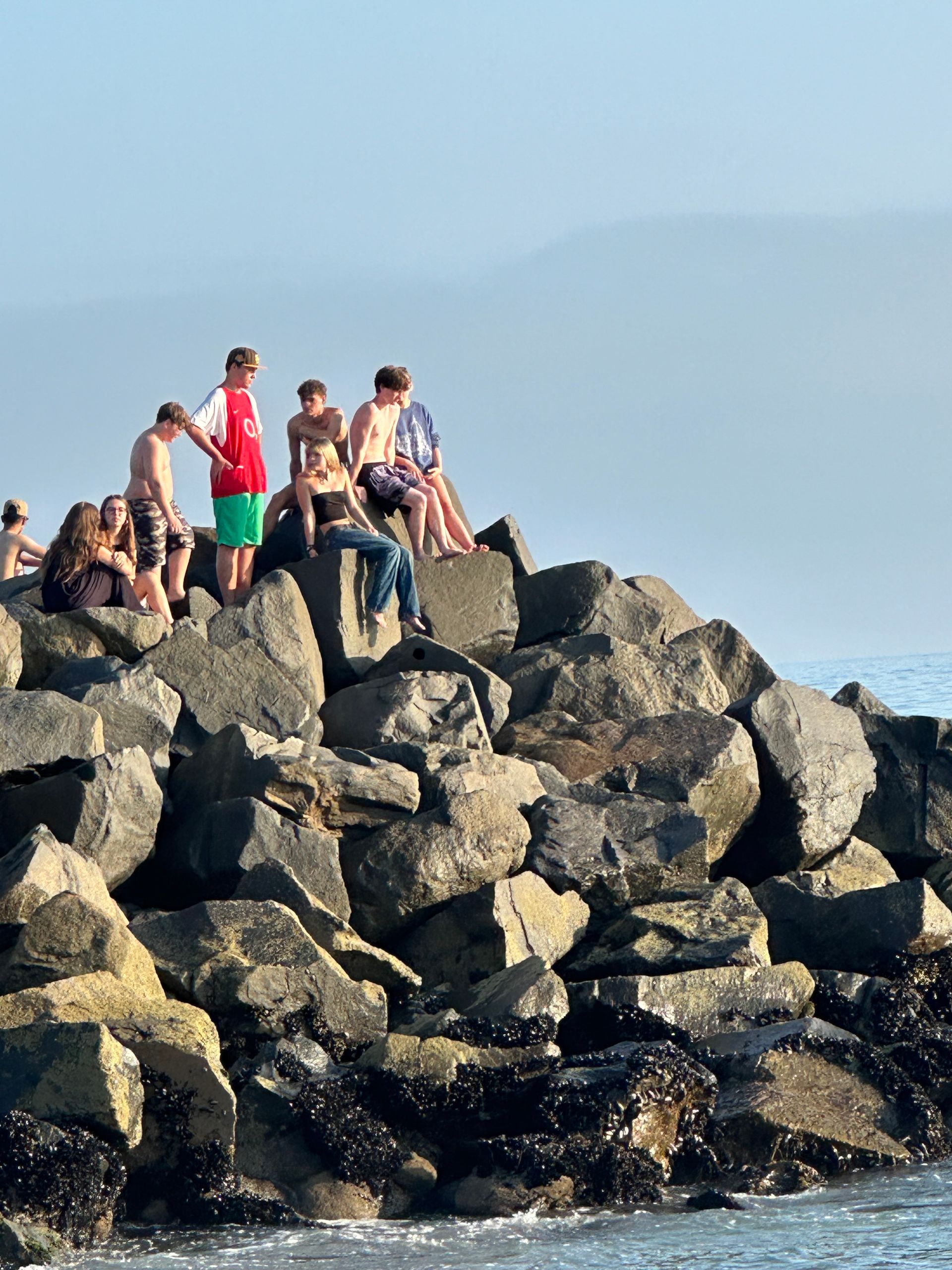 A group of people sitting on rocks near the ocean