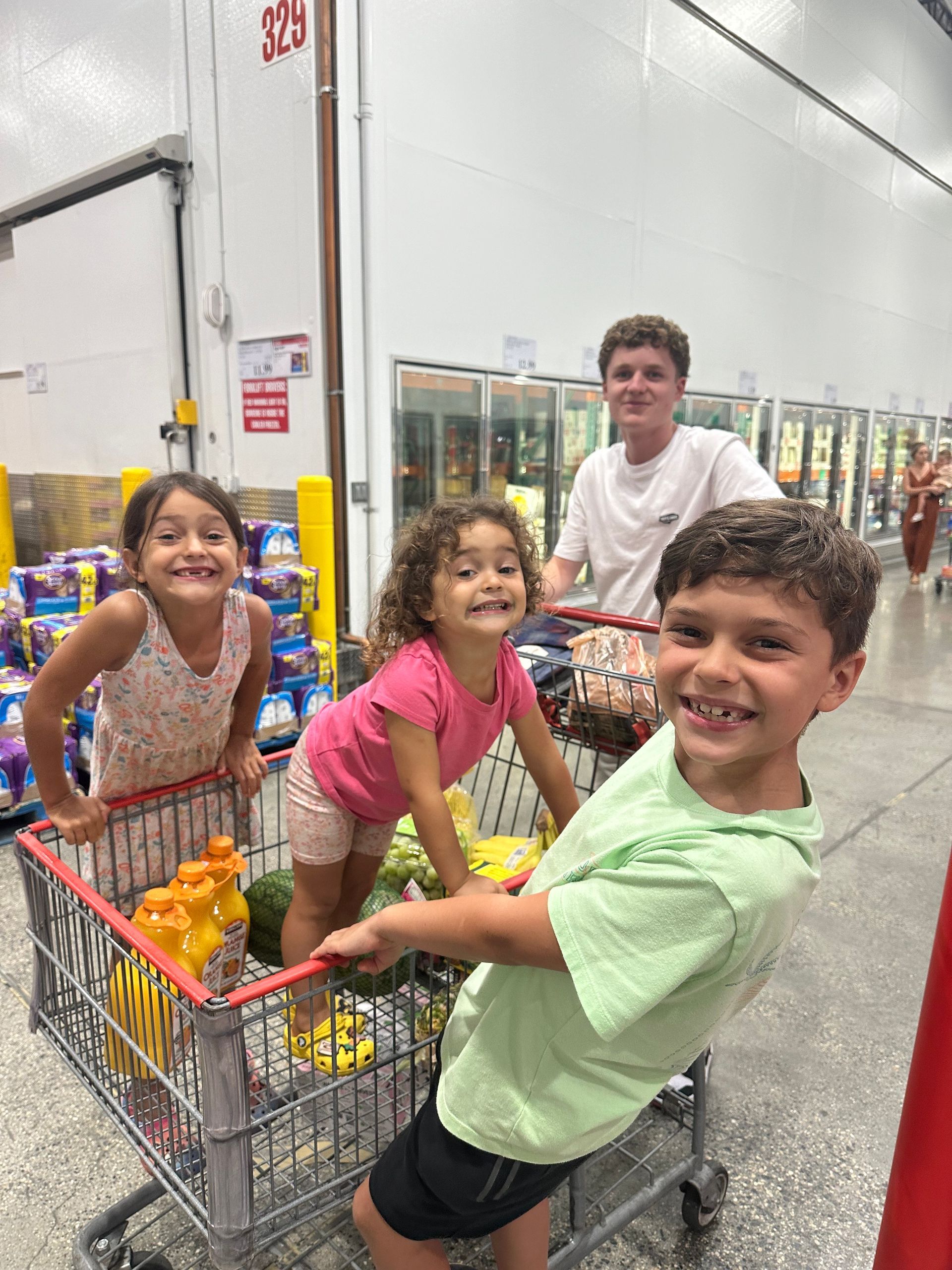 A group of children are pushing a shopping cart in a grocery store.