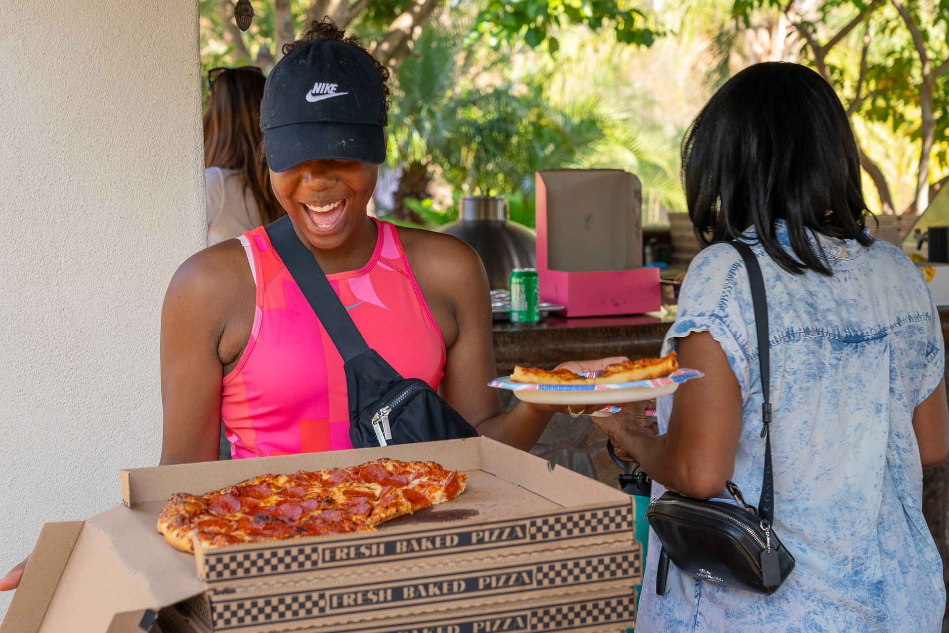 A woman is holding a box of pizza and another woman is holding a plate of pizza.
