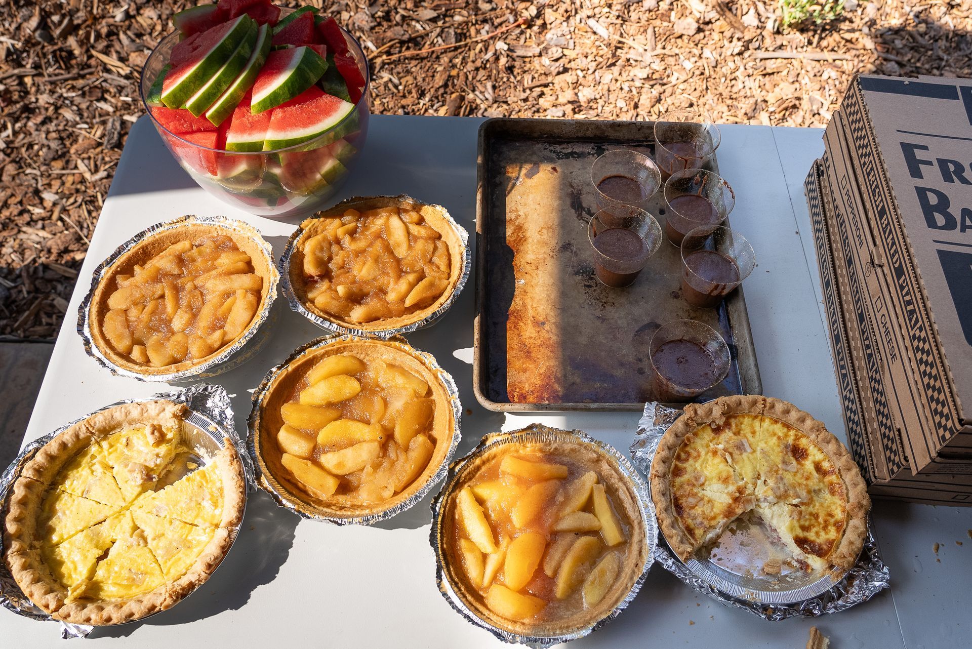 A table topped with a variety of pies and a box of watermelon