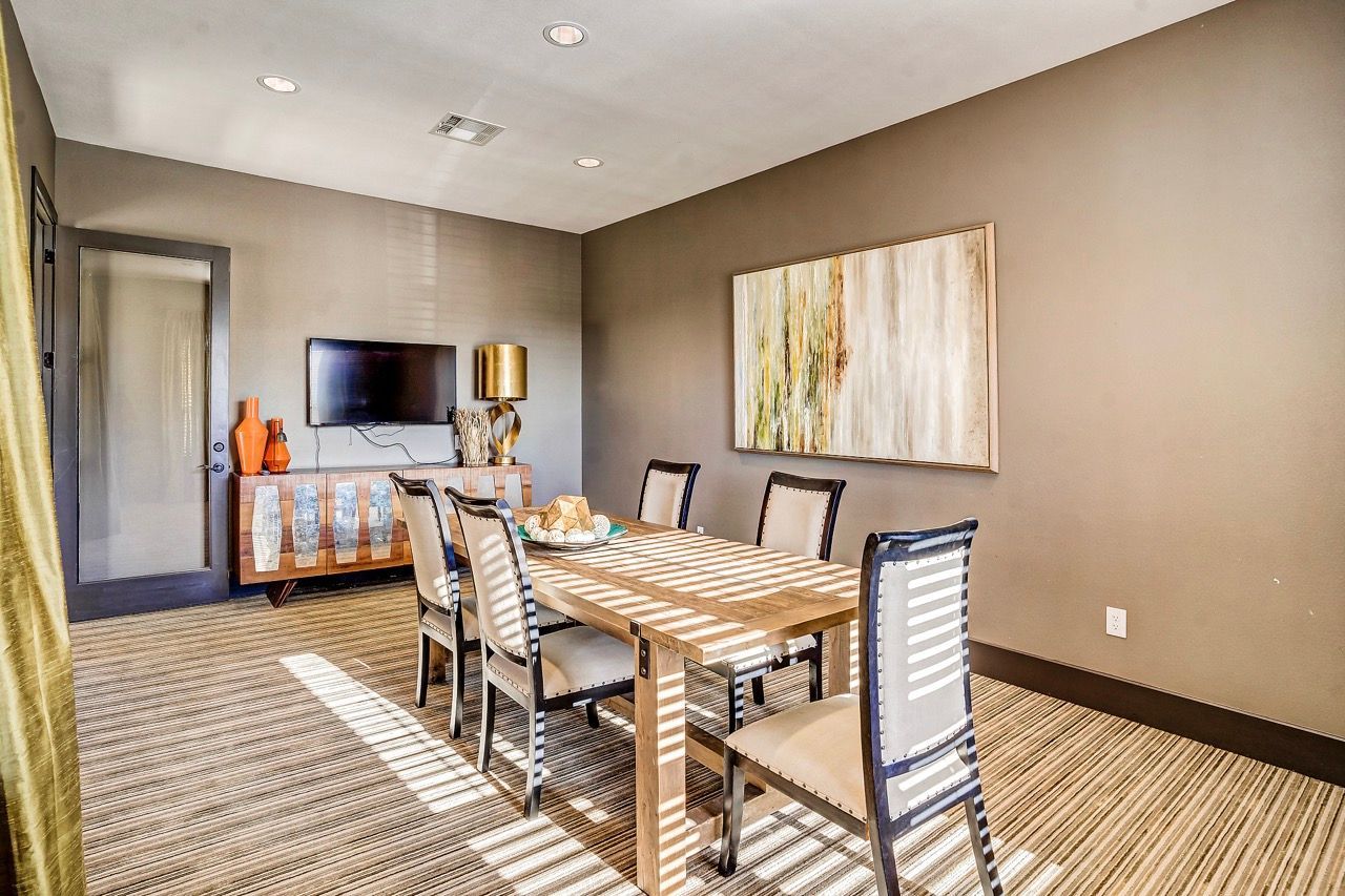 Dining room in an apartment with a wooden table, six upholstered chairs, and a wall-mounted TV.