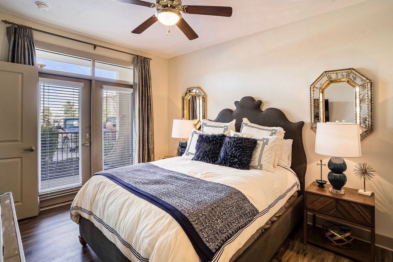 Bedroom in an apartment with an upholstered bed, two nightstands, lamps, and glass doors to a patio.