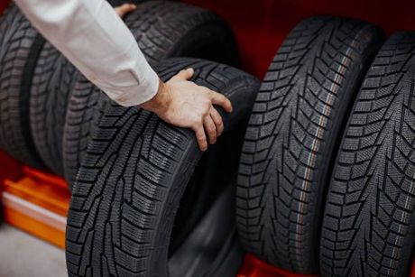 A person is holding a tire in front of a stack of tires.