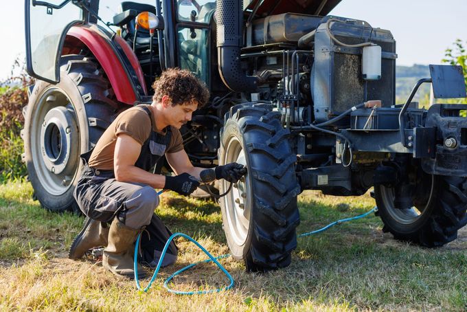 A man is changing a tire on a tractor in a field. A man is changing a tire on a tractor in a field.