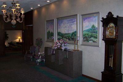 Hotel lobby with paintings, a grand clock, chandelier, and seating area