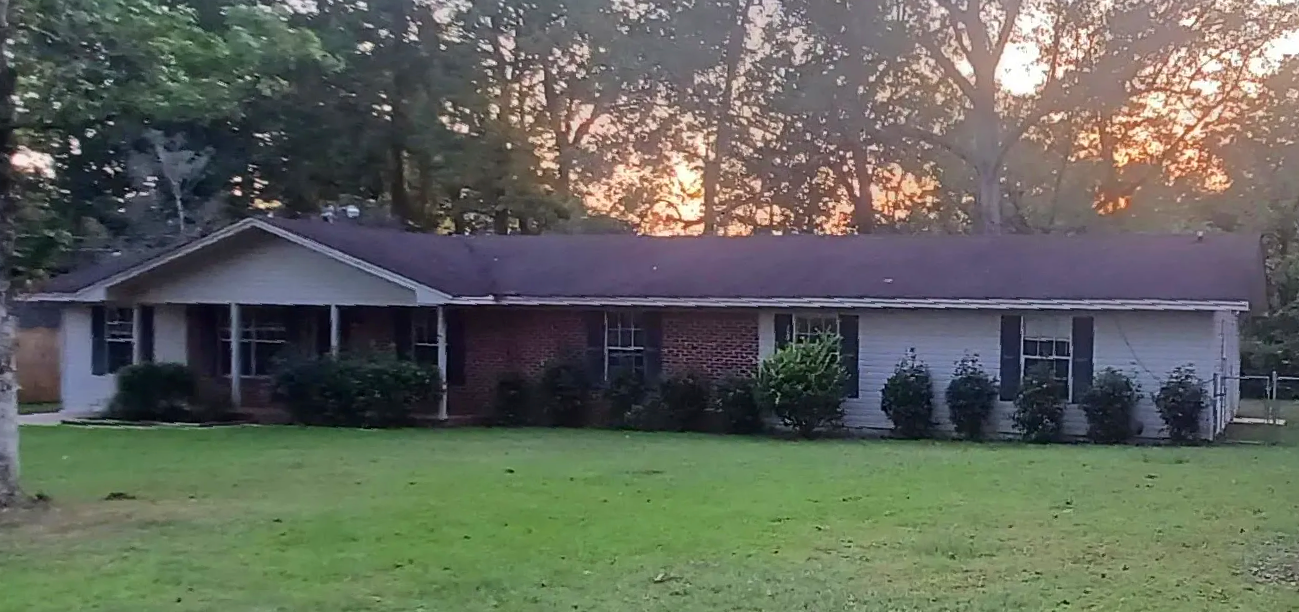 A large white house with a purple roof is surrounded by trees and grass.