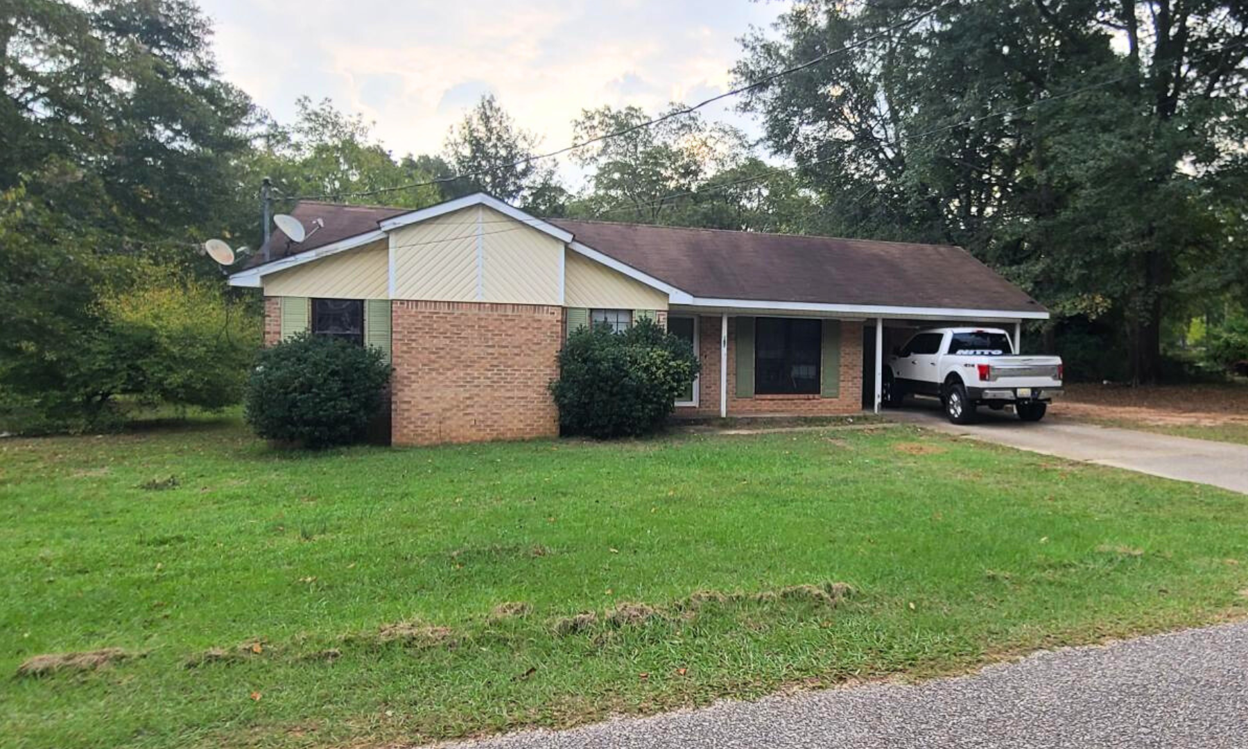 A white truck is parked in front of a brick house.