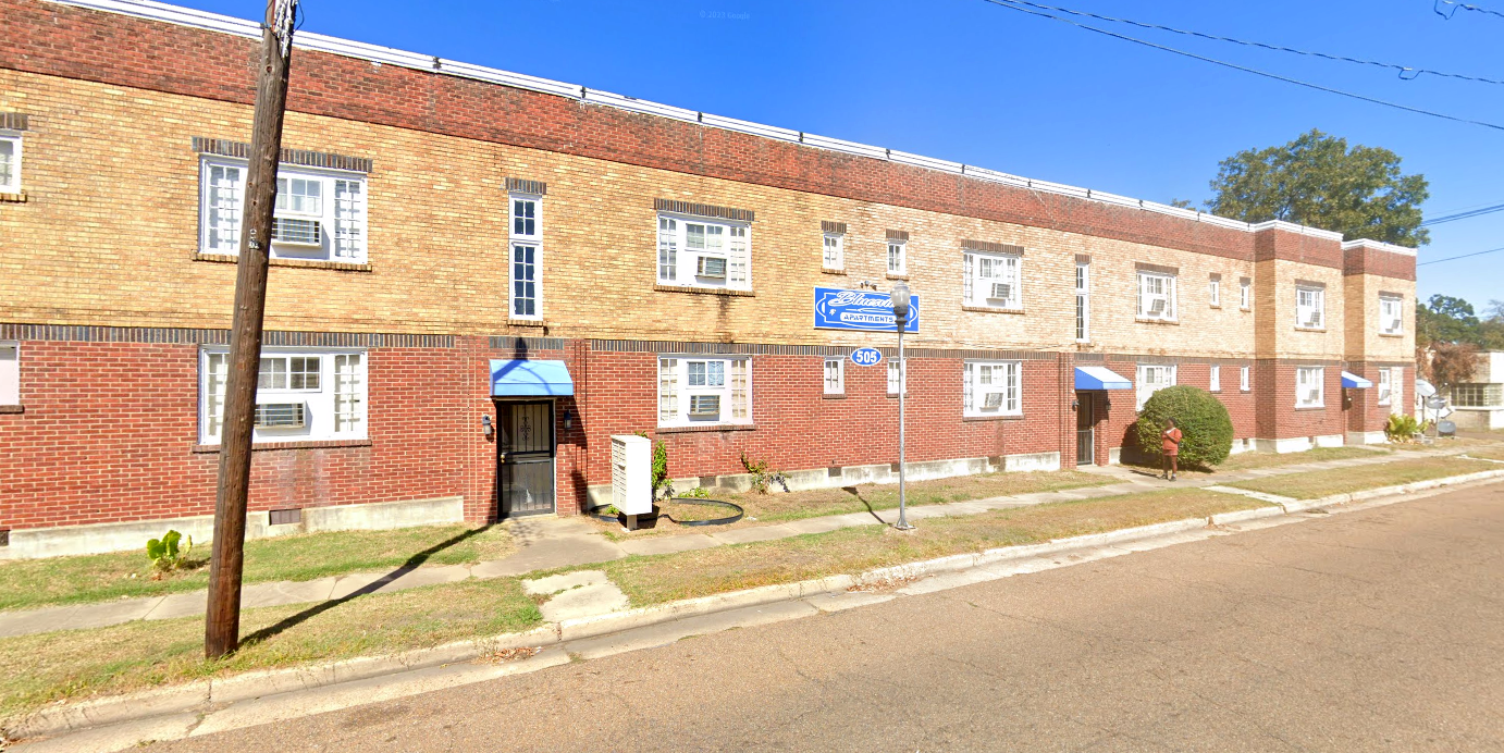 A brick apartment building with a blue awning on the front of it.