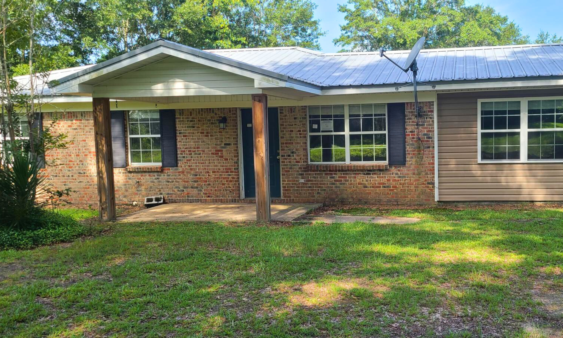 A brick house with a porch and a satellite dish on the roof.