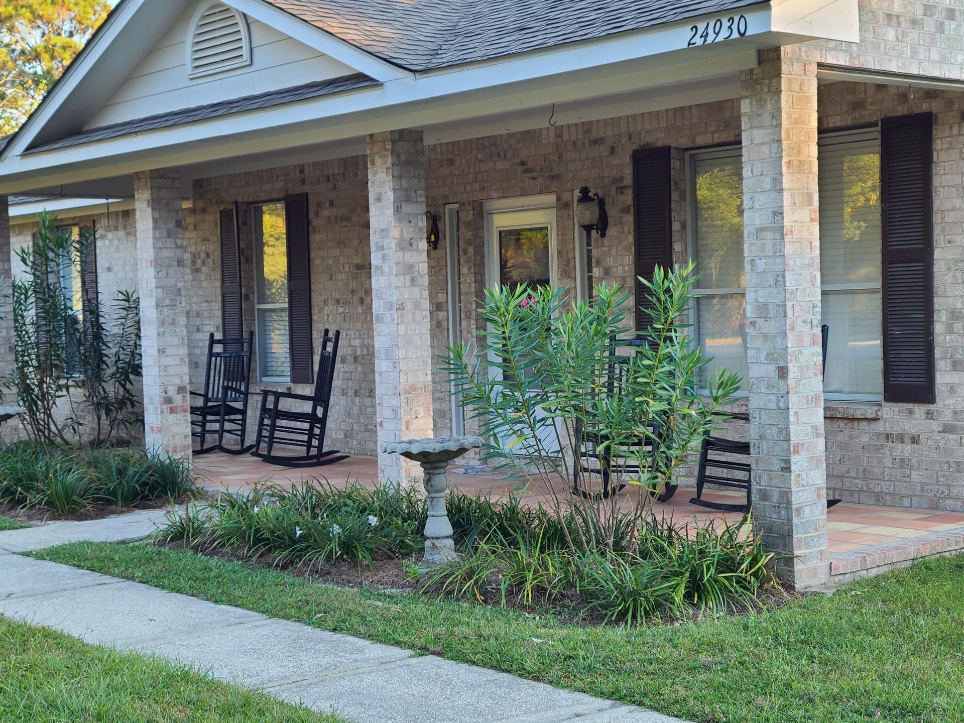 A brick house with a porch with rocking chairs and a bird bath.