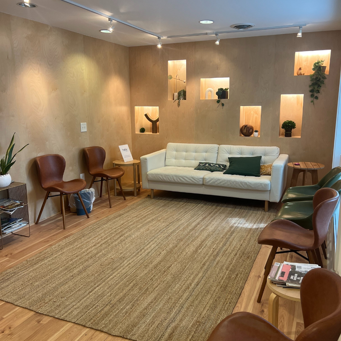 Waiting room with a white couch, brown chairs, and a jute rug. Beige walls with decorative niches.