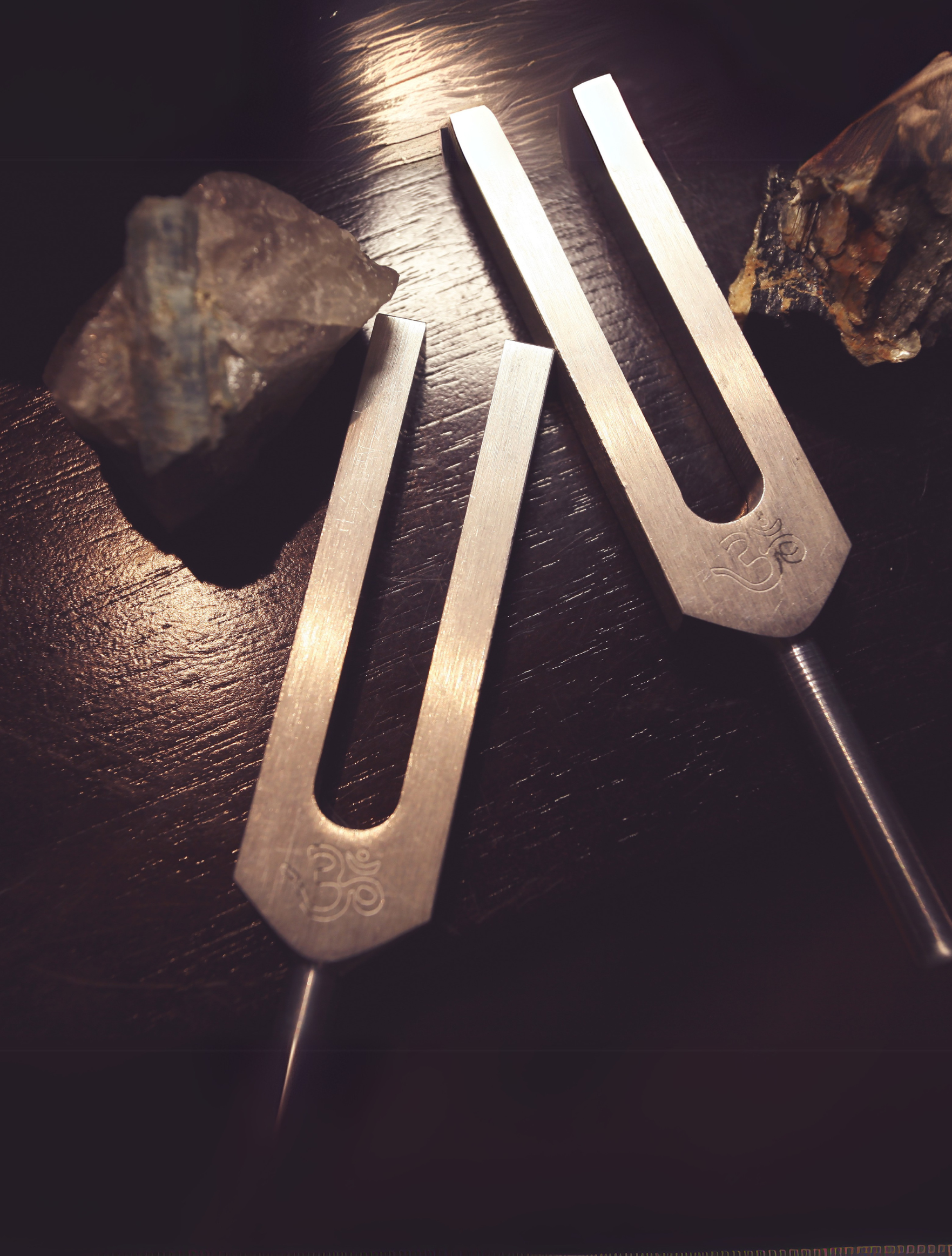 Three metal tuning forks next to rocks on a dark surface.