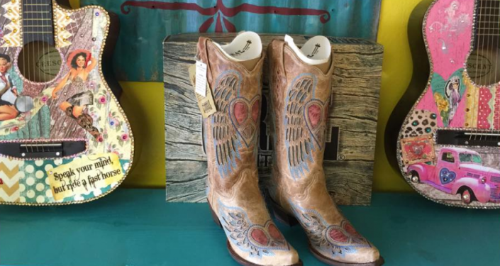 Decorative cowboy boots displayed between colorful painted guitars on a teal surface