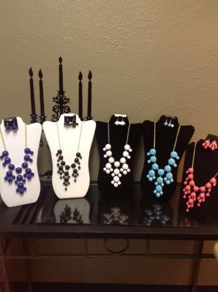 Five beaded necklace displays on black and white busts atop a table
